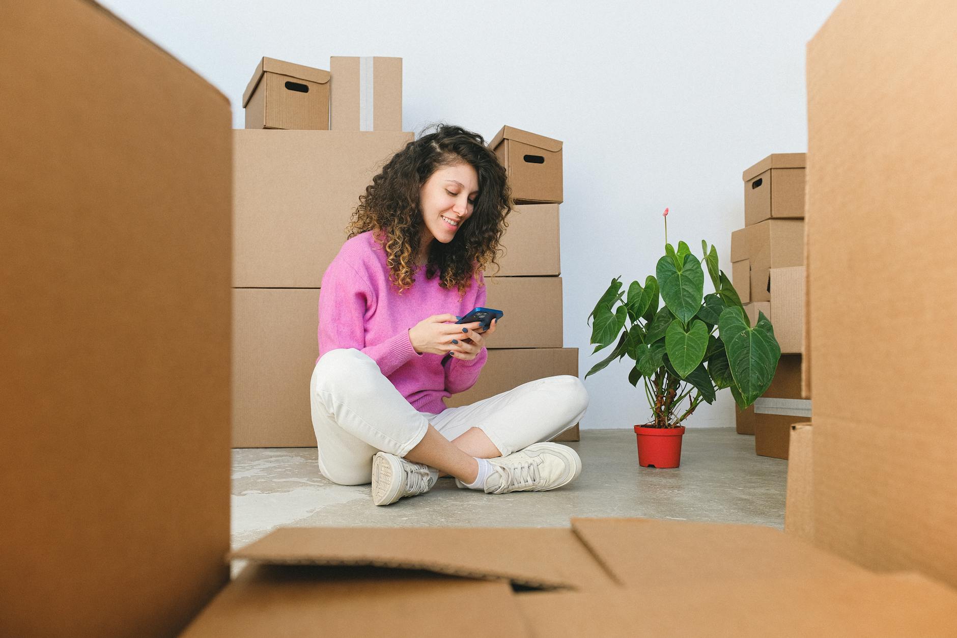 Cheerful woman checking her phone, surrounded by unpacked moving boxes in a cozy indoor setting.