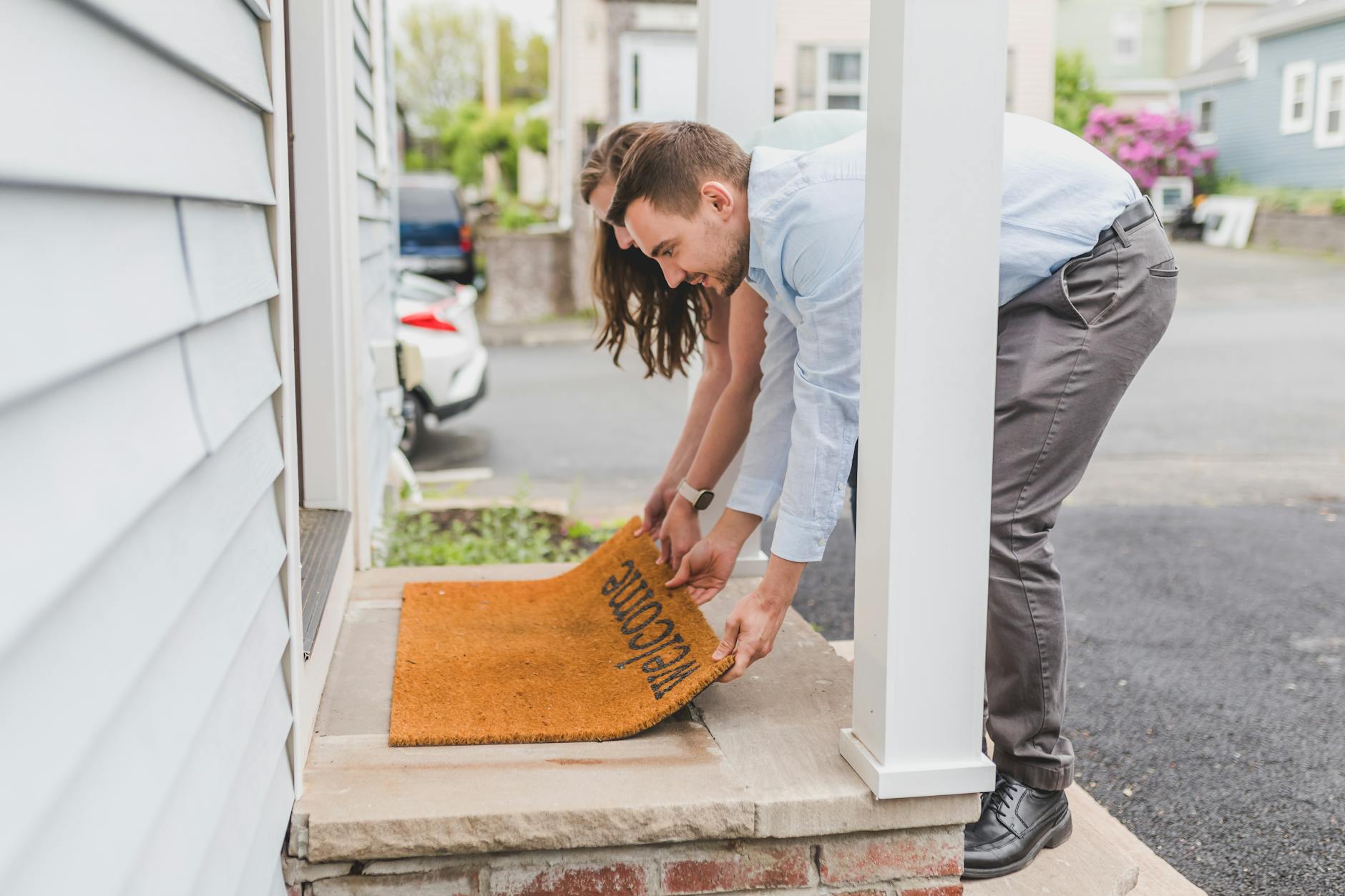 A young couple placing a welcome mat on their new home's porch, representing new beginnings.