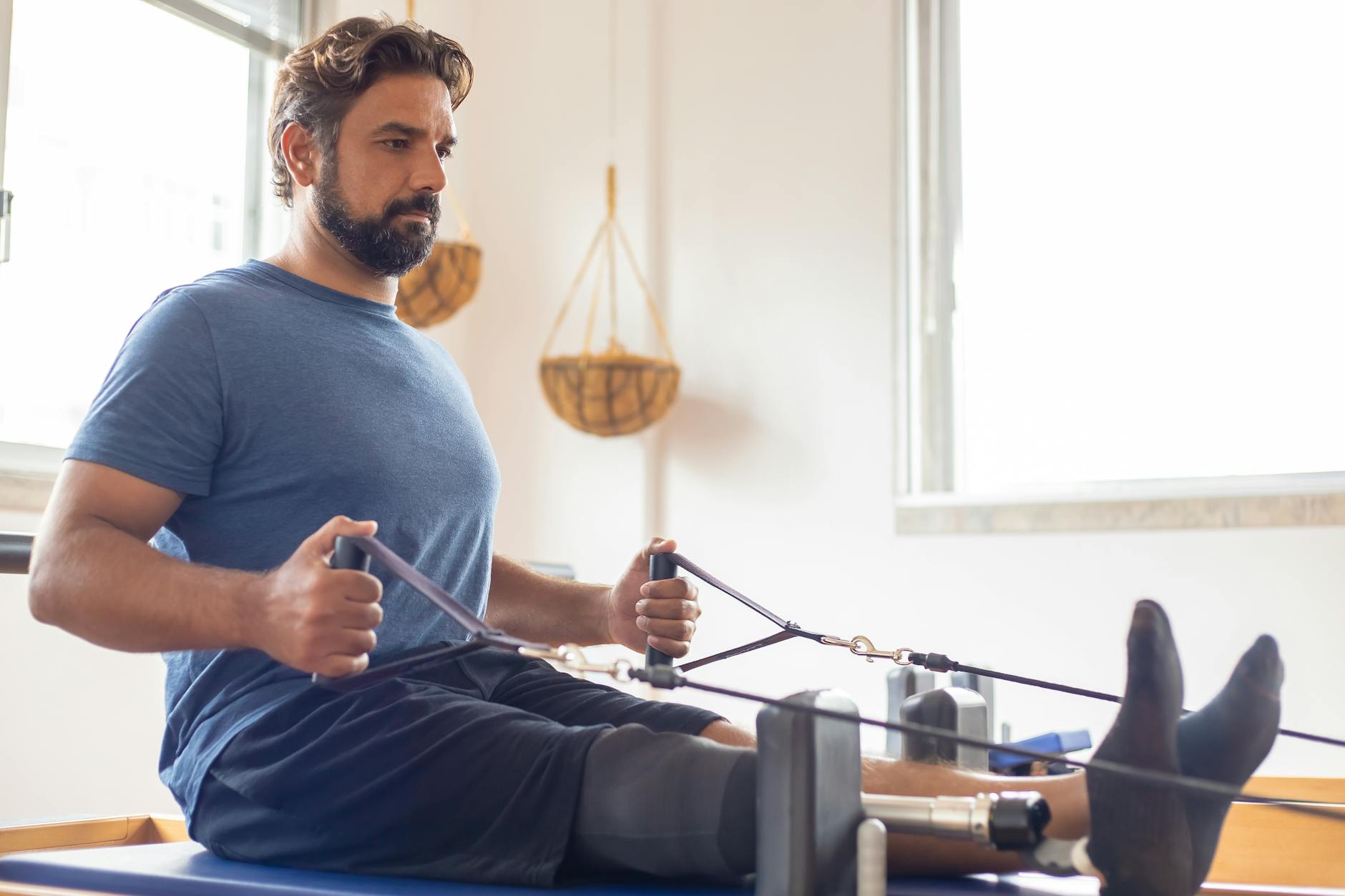 Man with a prosthetic leg practicing Pilates exercises indoors, focusing on strength and rehabilitation.