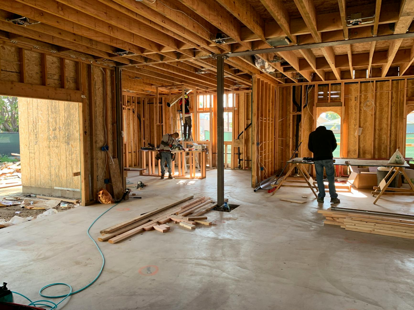 Construction workers framing a house, with wooden beams and scaffolding visible in the process.