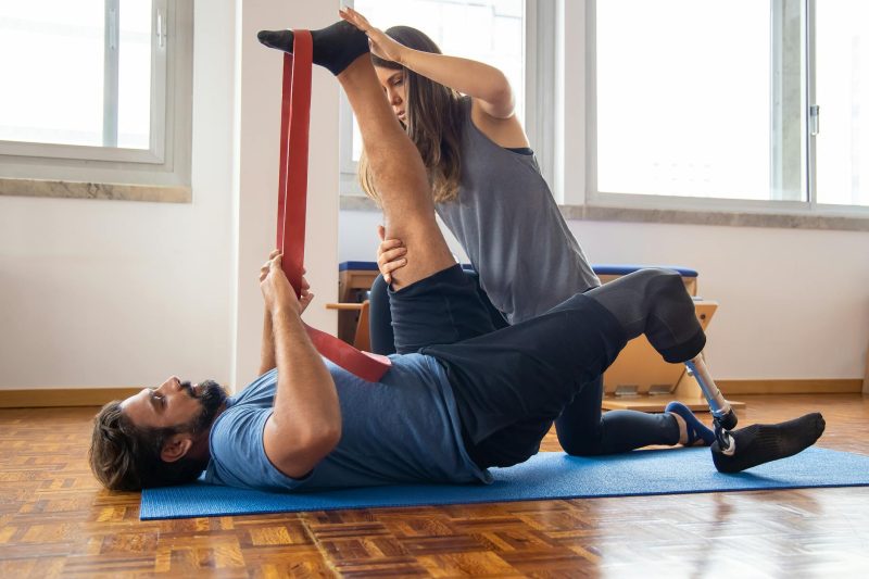 Man exercises with a trainer, focusing on rehabilitation with a prosthetic leg in a bright gym setting.