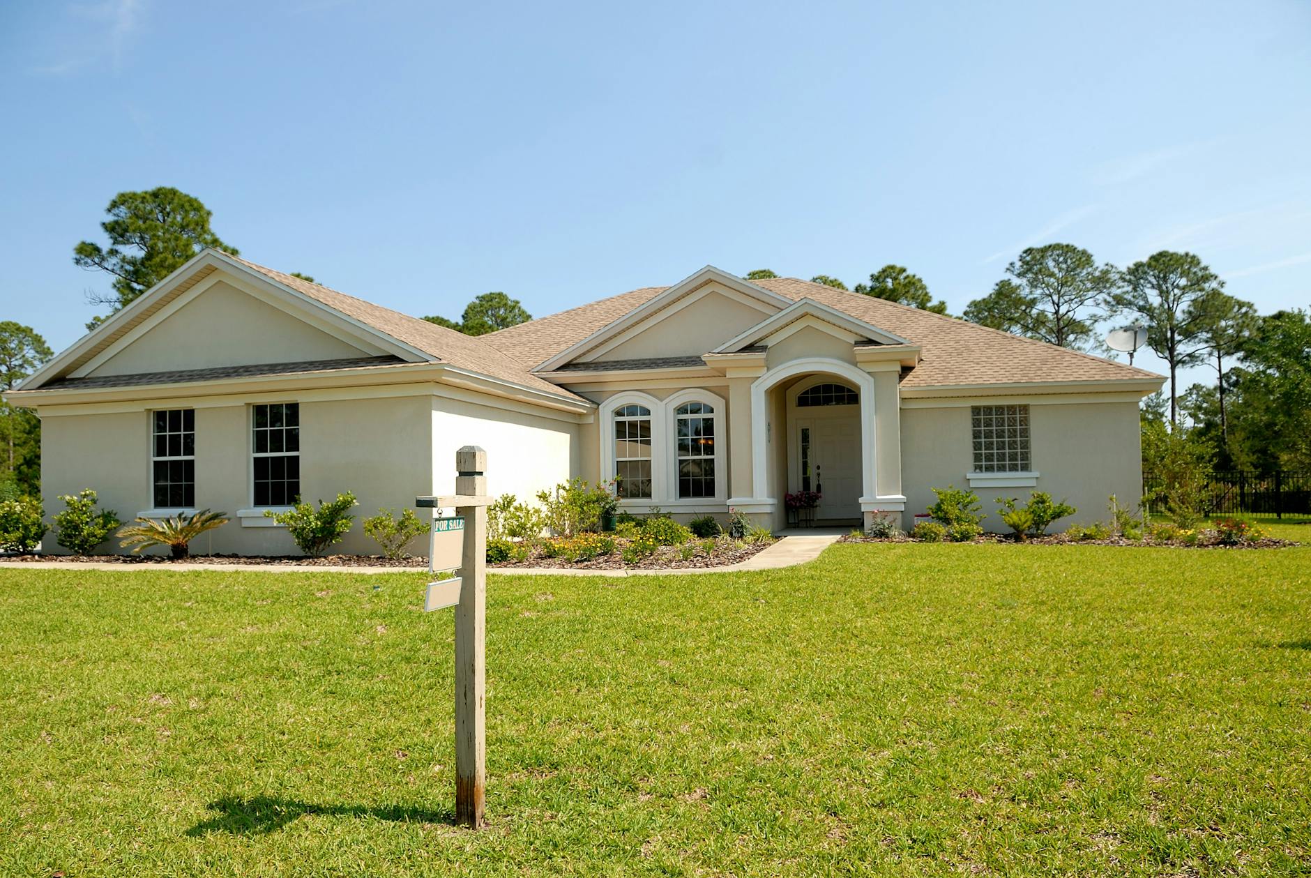 Suburban house with a lush lawn and a for sale sign beneath a clear blue sky.