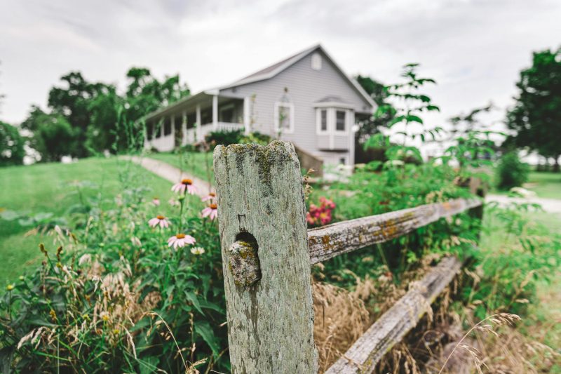 A charming rural house with a vibrant flower garden and wooden fence.