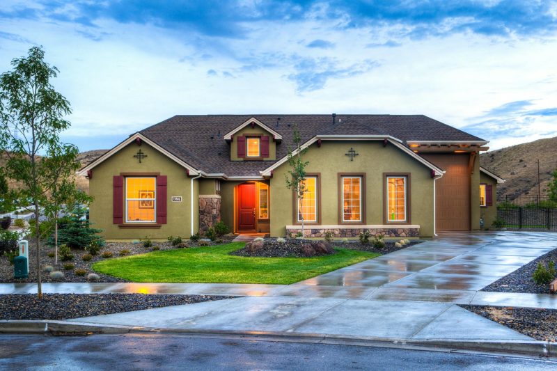 Modern home exterior with illuminated facade, lush green lawn, and wet driveway in Boise.
