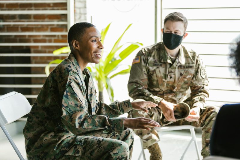 Soldiers in military uniforms engaged in conversation during an indoor therapy session.