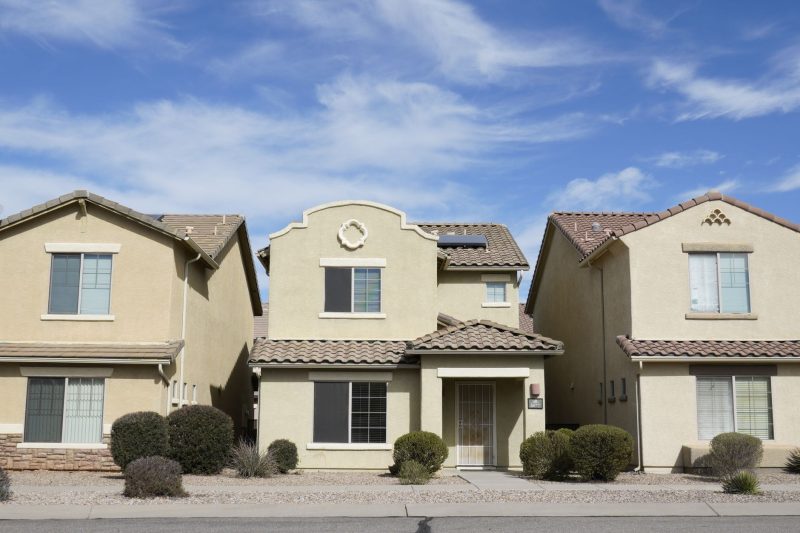 Three similar suburban houses with manicured lawns in Tucson, Arizona, under a clear blue sky.