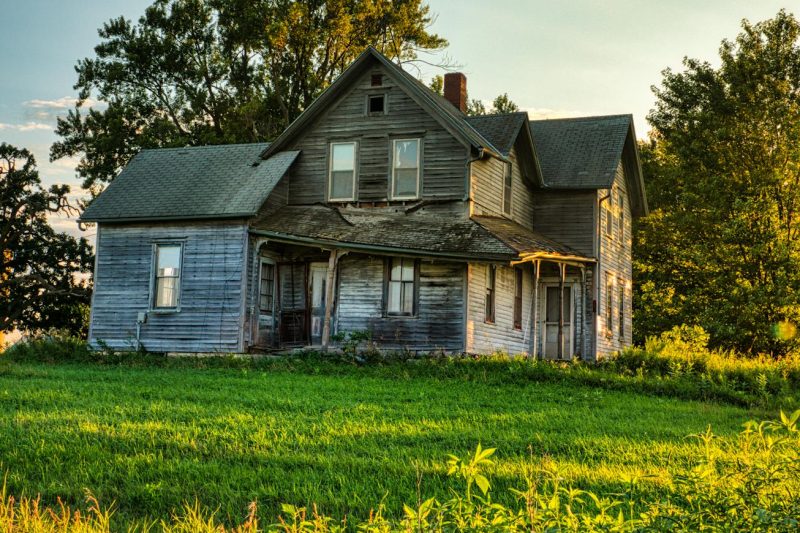 Rustic wooden farmhouse nestled among lush green summer foliage.