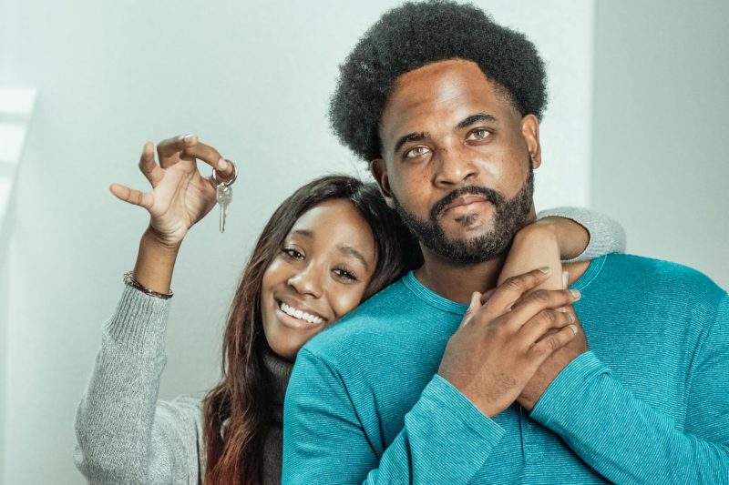 Smiling couple indoors joyfully holds house keys, surrounded by a cozy home setting.