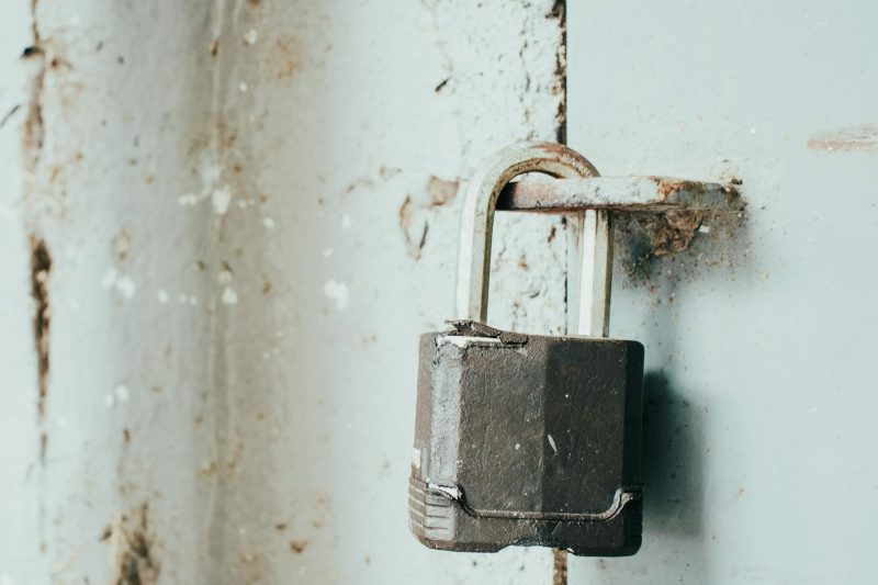 Close-up of a rusty padlock on a weathered door, emphasizing its age and textured surface.