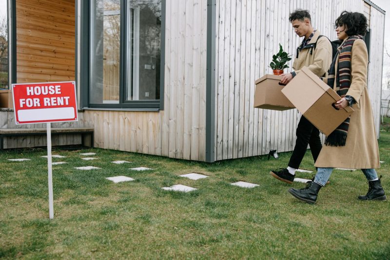Young couple carrying boxes into a newly rented house, symbolizing moving and new beginnings.