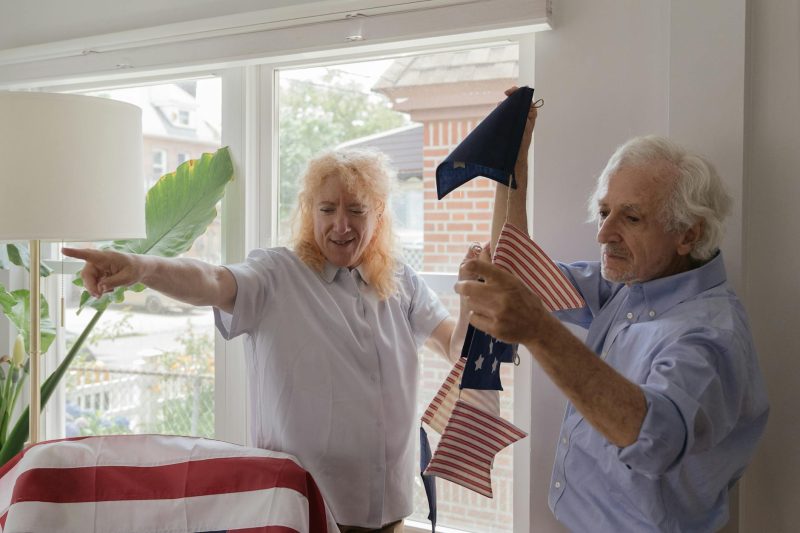 Elderly couple arranging American flags together at home, smiling and engaged in a patriotic celebration.
