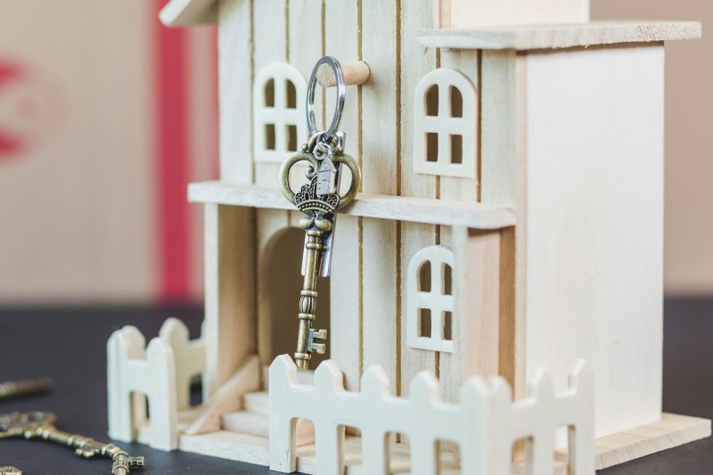 Miniature wooden house beside a vintage key on a neutral background.