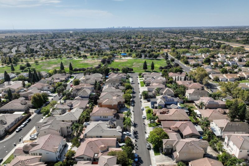 Aerial view of a sunny Sacramento suburb featuring rows of houses and abundant greenery.
